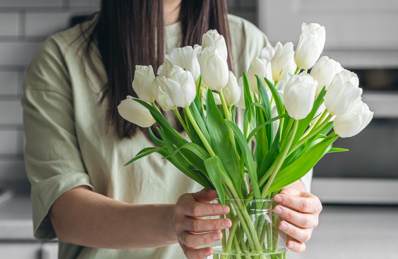 woman-putting-bouquet-white-tulip-flowers-into-vase-kitchen 1.jpg